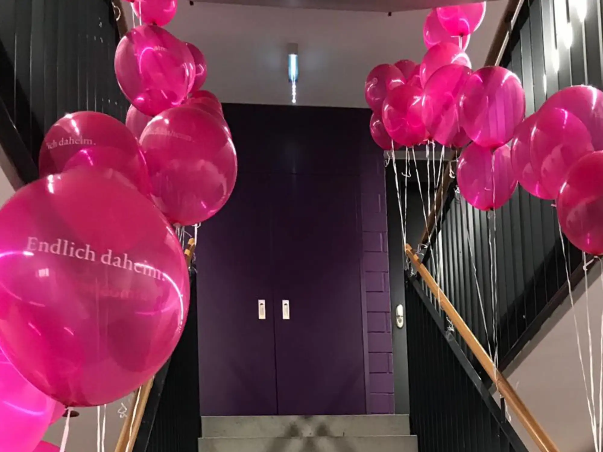 Treppenaufgang in einem Bürogebäude mit vielen pinken Luftballons an den Geländern.