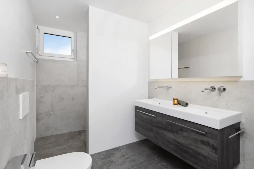 Modernes Kinderbad mit bodengleicher Dusche, hellem Naturstein, Doppelwaschbecken und großem Spiegelschrank.