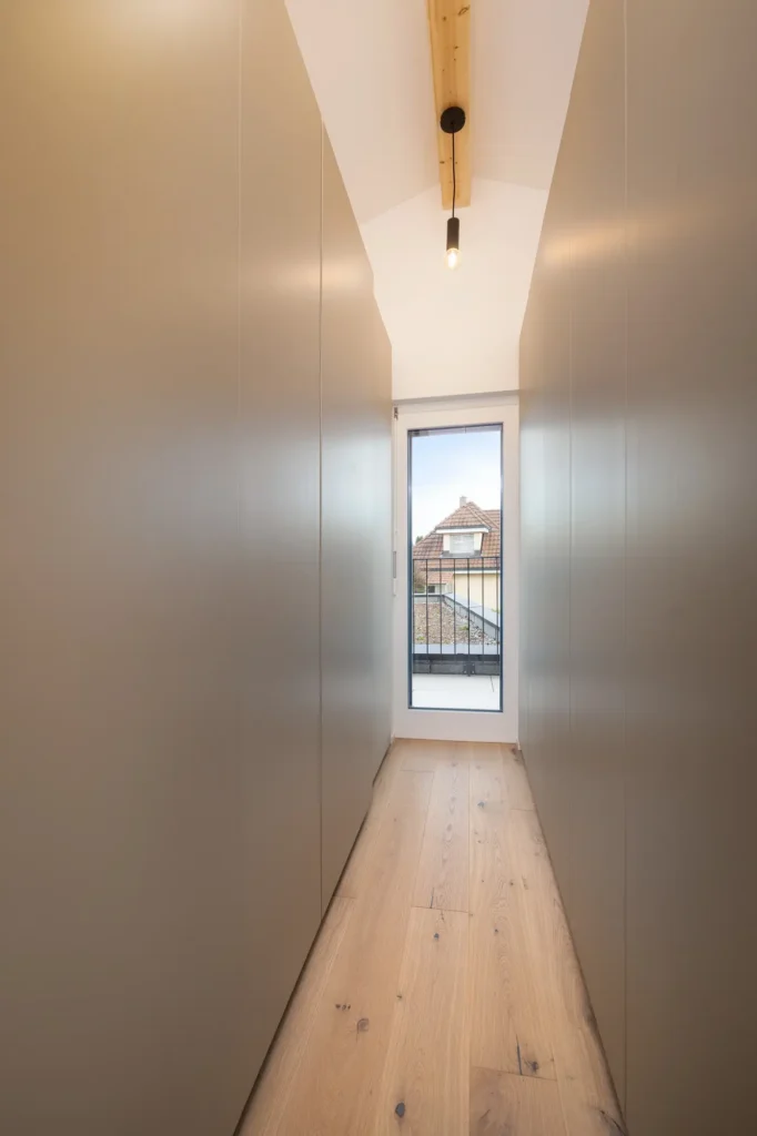 Schmale Ankleide mit beidseitigen Schrankfronten, Holzdecke und Fenster am Raumende.