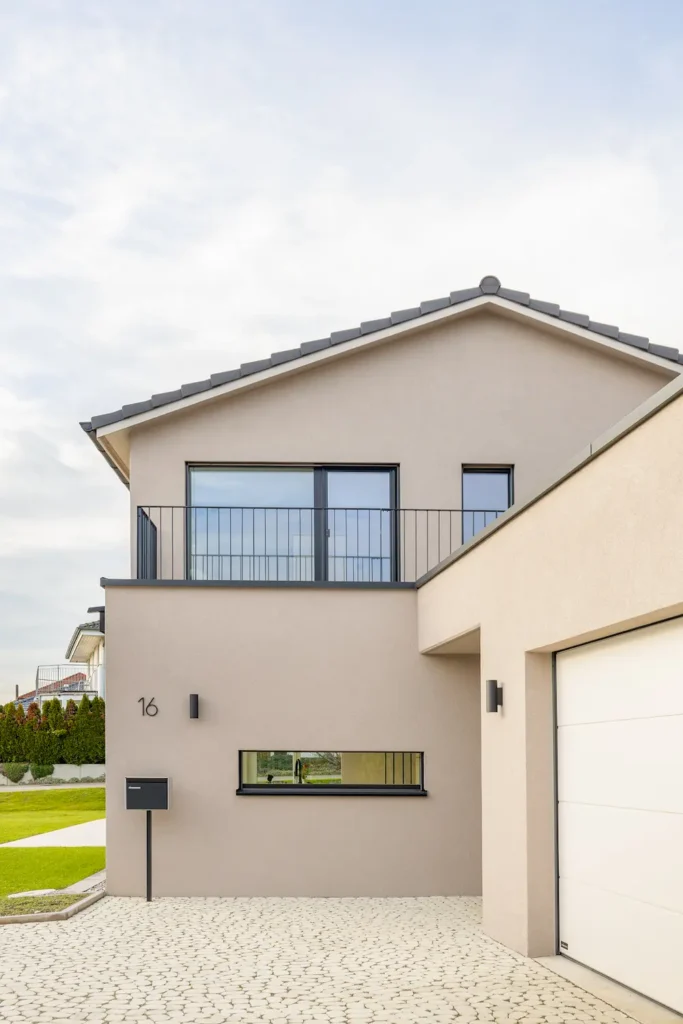 Moderner Hauseingang eines Einfamilienhauses mit Balkon, klarer Fassadengestaltung und integrierter Garage.