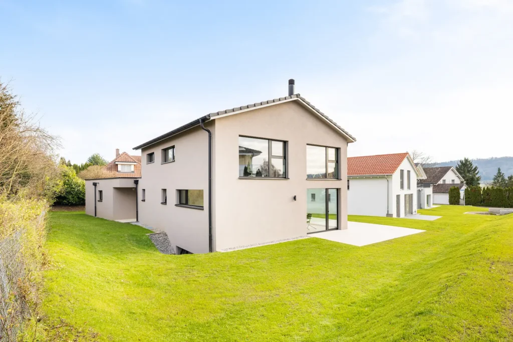 Rückansicht eines modernen Einfamilienhauses mit Satteldach, grossem Garten und bodentiefen Fenstern.