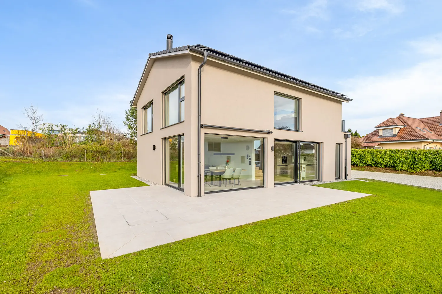 Modernes Einfamilienhaus mit klarer Kubatur, bodentiefen Verglasungen und fliessendem Übergang von innen nach aussen.