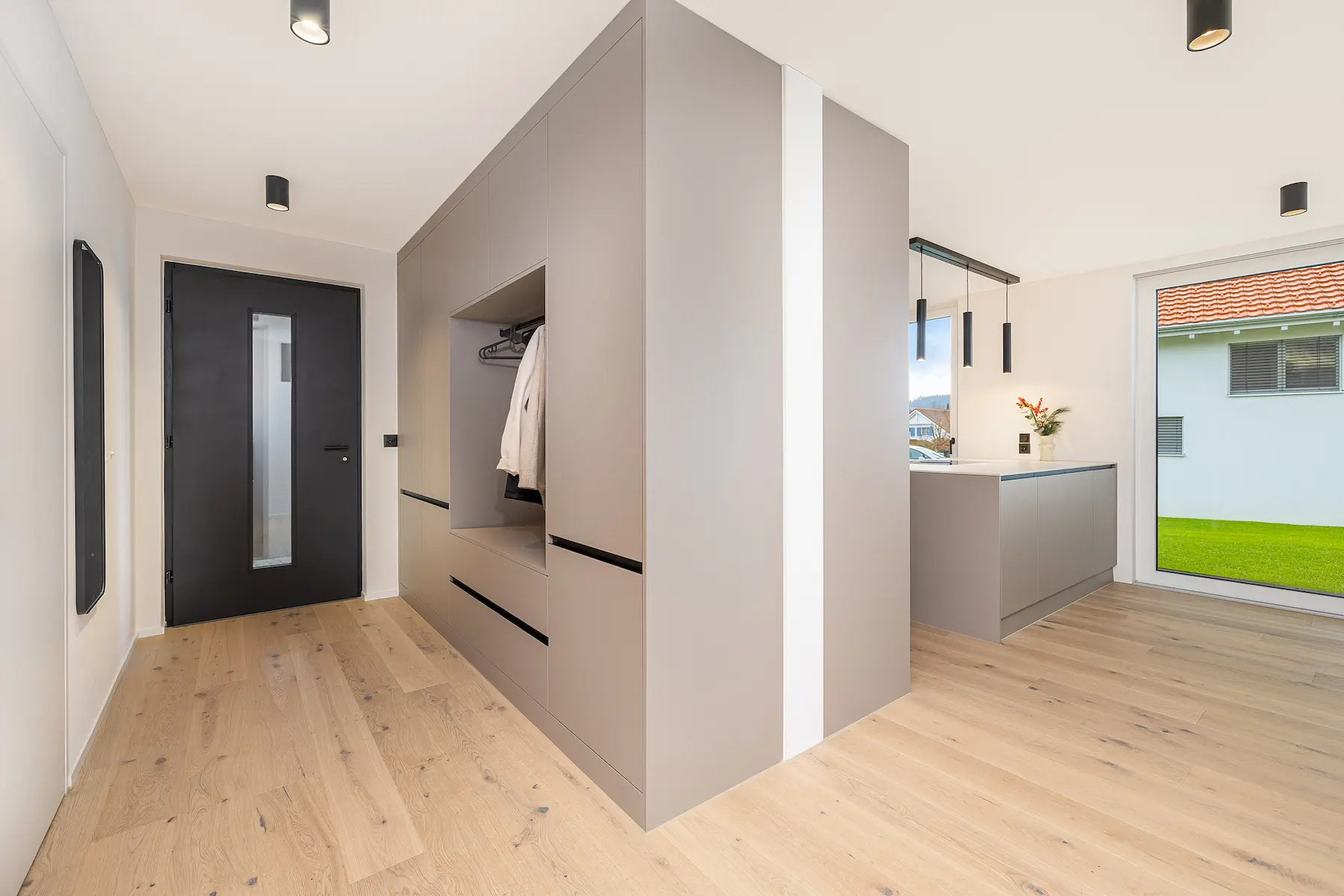 Hauseingangstüre von innen mit Entrée mit integrierter Garderobe, massgefertigten Einbauten und offenem Übergang zur Küche.
