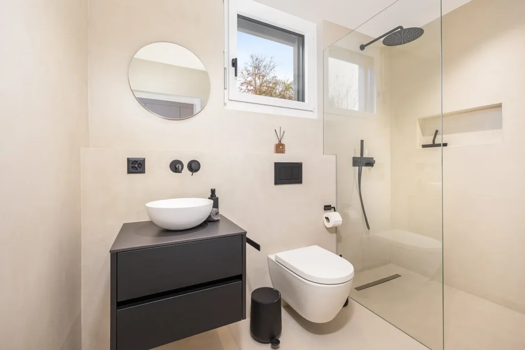 Gästebad mit Waschbecken in dunklem Holz, WC, integrierter Beleuchtung, Dusche und schwarzen Armaturen.