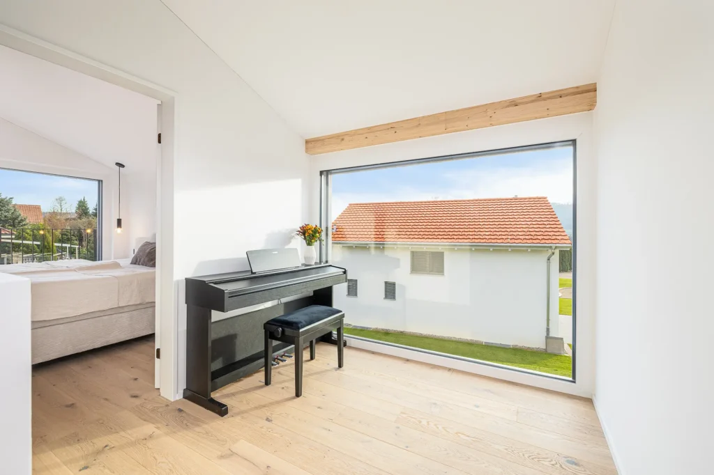 Galeriebereich mit grosser Fensterfront, schwarzem Piano, Holzdetails und Blick in den angrenzenden Schlafraum.