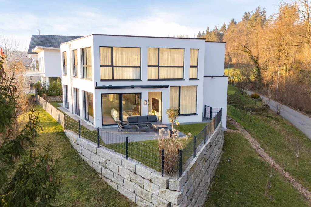 Modernes Einfamilienhaus mit Flachdach, großen Fenstern und Terrasse in Hanglage.