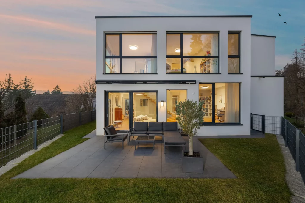 Modernes Einfamilienhaus mit beleuchteten Fenstern und Terrasse bei Dämmerung.