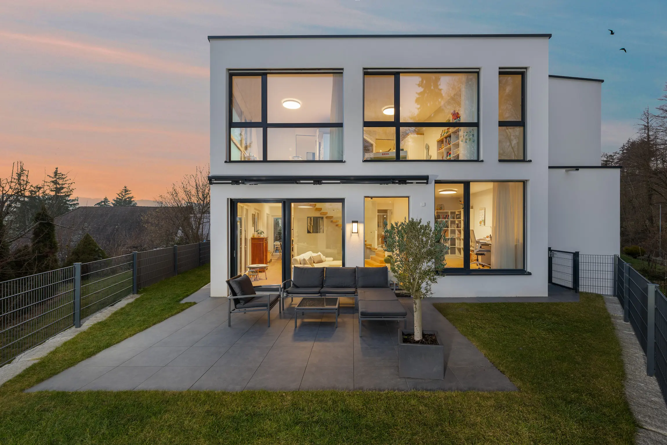 Modernes Einfamilienhaus mit beleuchteten Fenstern und Terrasse bei Dämmerung.