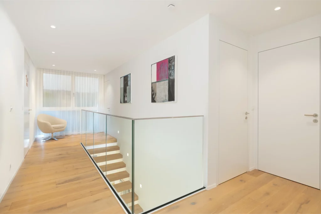 Heller Flur im Obergeschoss mit Treppe und Glasgeländer.