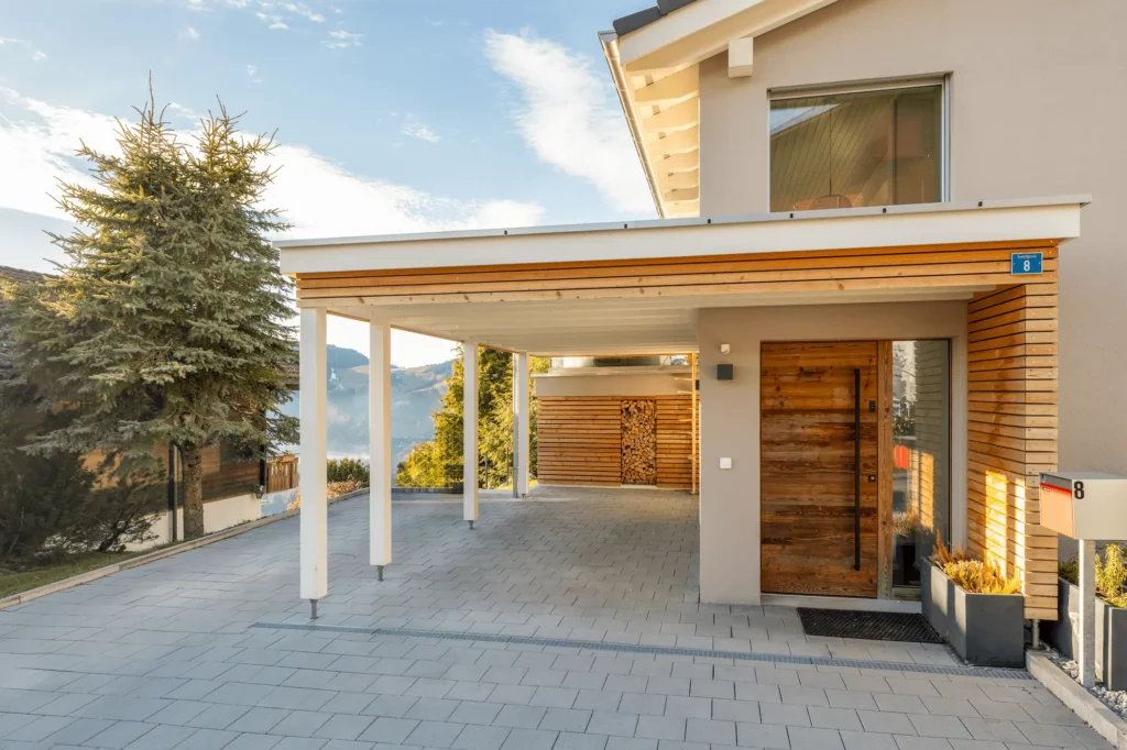 Moderner Carport mit Flachdach, Holzlamellen und direktem Zugang zum Einfamilienhaus.