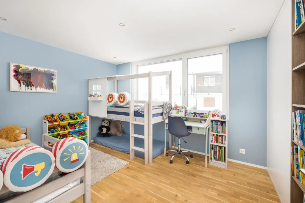 Helles Kinderzimmer mit Hochbett, Schreibtisch und Stauraum.
