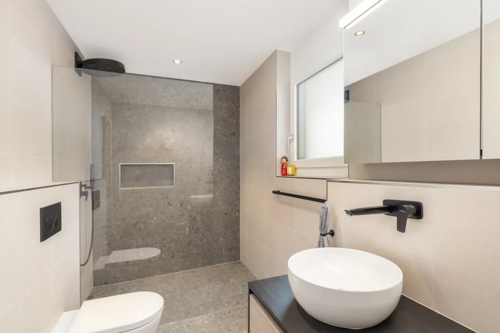 Modernes, beiges Badezimmer mit bodengleicher Dusche, Waschtisch und WC.