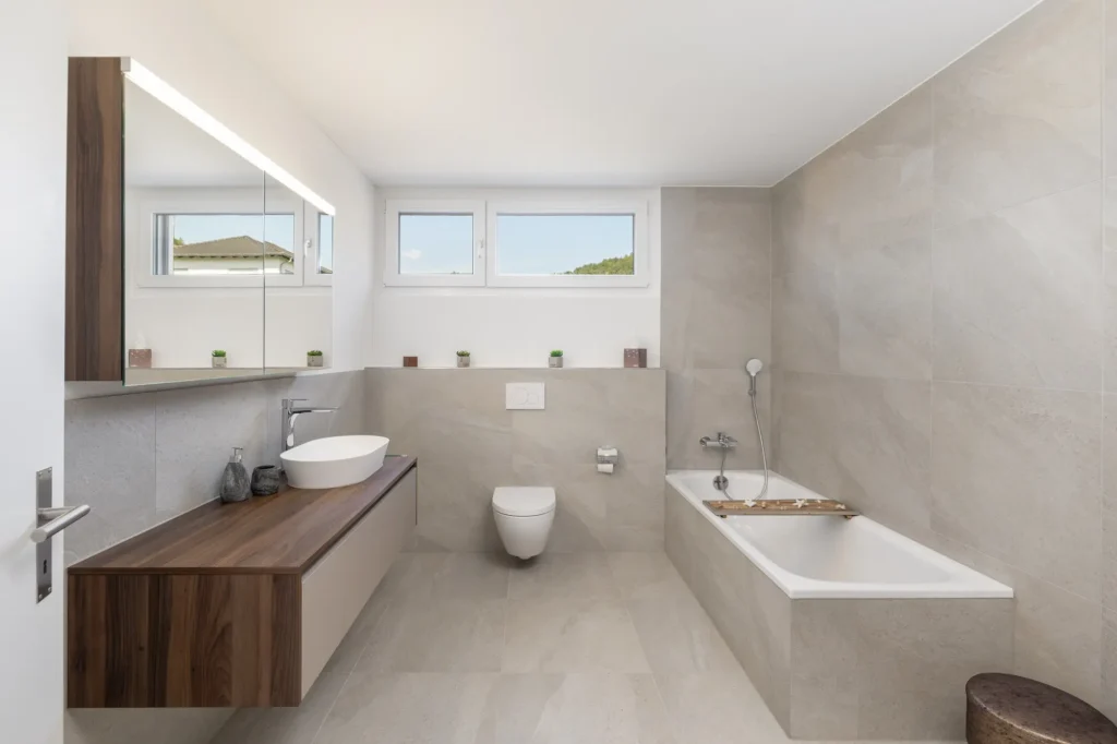 Badezimmer mit Badewanne, wandhängendem WC, Waschtisch mit Holzabdeckung und Fensterband.