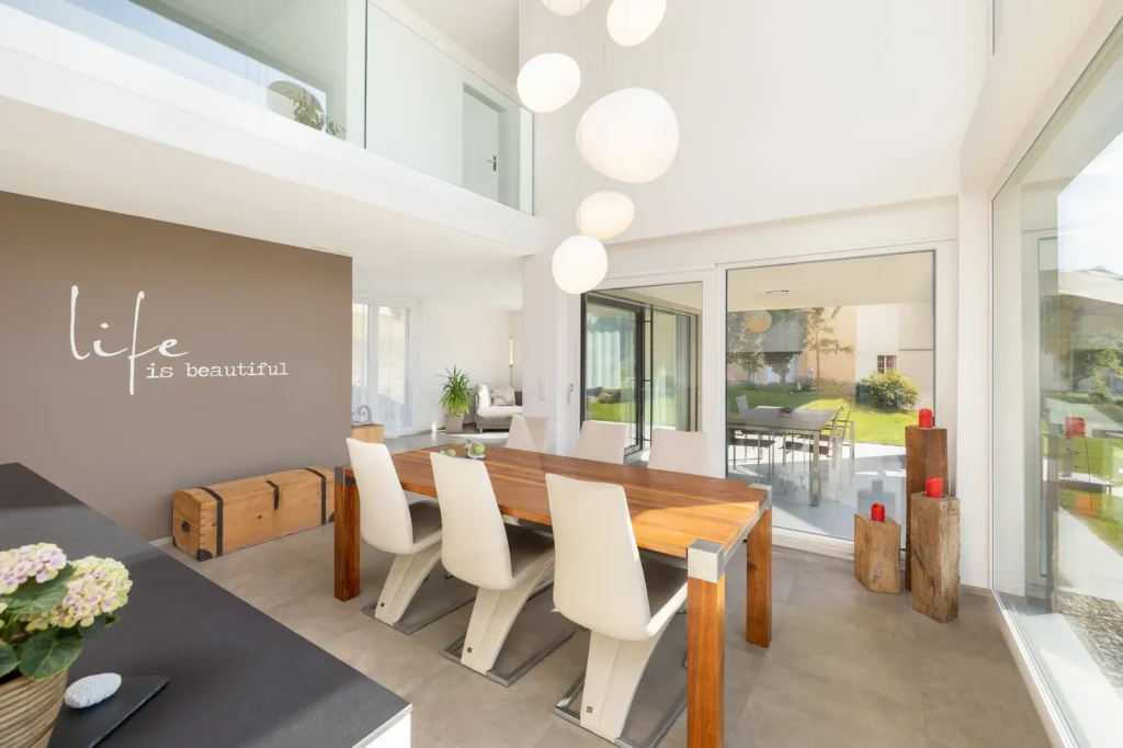 Offener Essbereich mit Holztisch, Stühlen, Pendelleuchten, Galerie und grossen Fensterfronten mit Zugang zur Terrasse.