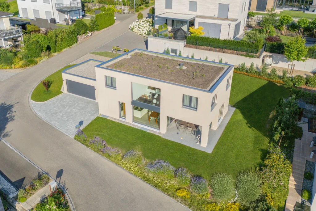 Luftaufnahme eines Einfamilienhauses mit Flachdach, angrenzender Garage, Terrasse und gepflegtem Garten.