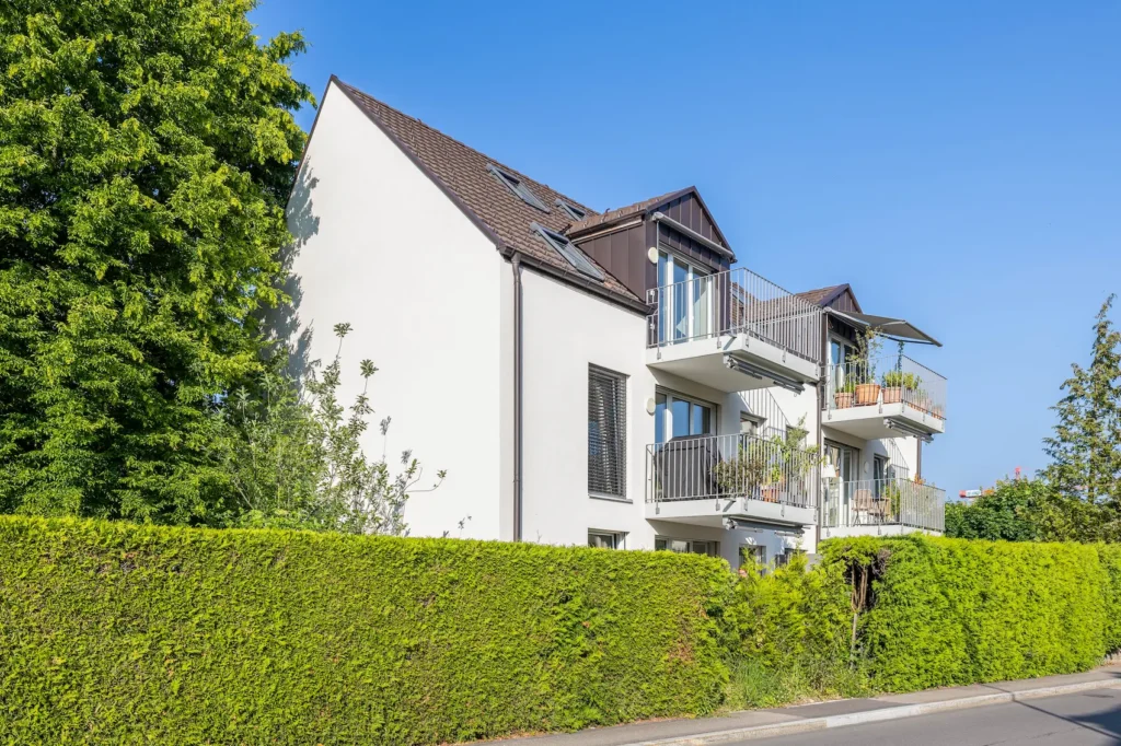 Mehrfamilienhaus mit klassischer Dachform und gestapelten Balkonen, Seitenansicht.