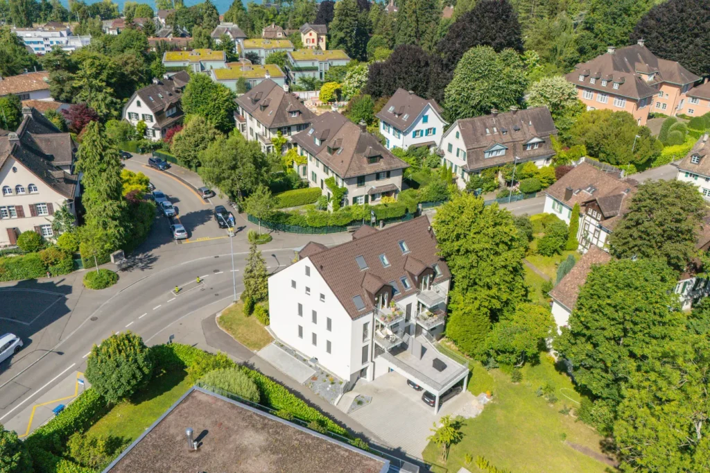 Luftaufnahme eines Mehrfamilienhauses in Zürich mit Balkonen, Parkierung und umliegendem Wohnquartier.