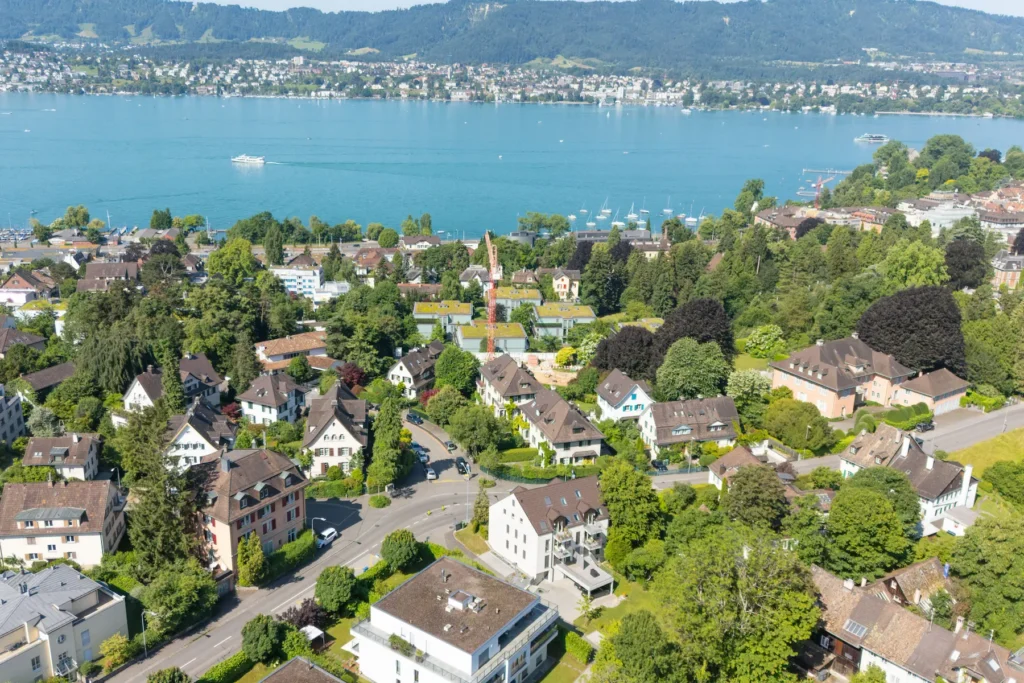 Luftaufnahme eines Zürcher Wohnquartiers mit Mehrfamilienhäusern, viel Grün und Blick auf den Zürichsee.