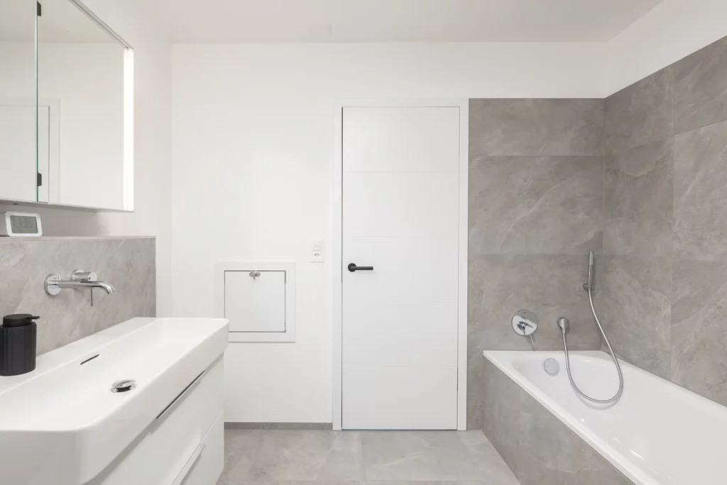 Badezimmer mit Wäscheabwurf, Badewanne, Waschbecken und Wandarmaturen.