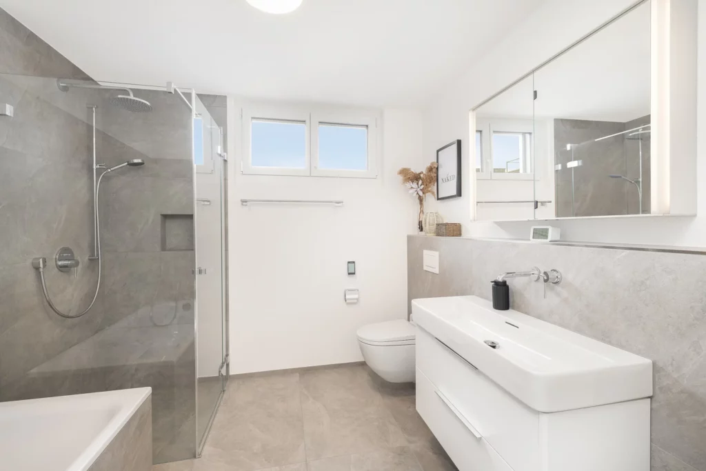 Helles Badezimmer mit Dusche, Waschbecken, Toilette und Tageslichtfenstern