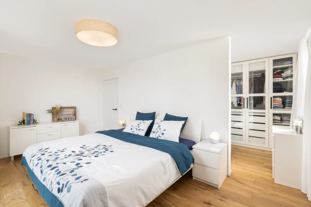 Helles Schlafzimmer mit Doppelbett, Holzfußboden und angrenzender Ankleide.