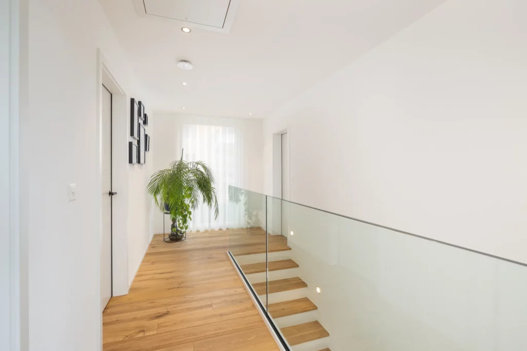 Heller Flur mit Holzfußboden, Glasgeländer und Treppe in einem Einfamilienhaus von Atmoshaus