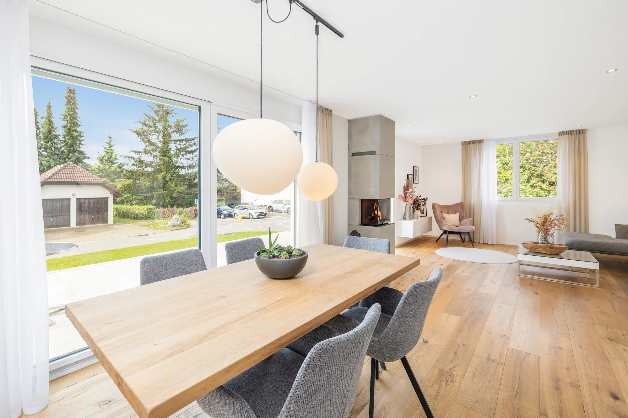Moderner Essbereich mit eleganten Möbeln, Holztisch, Holzboden, Kamin im Hintergrund und grosser Fensterfront.