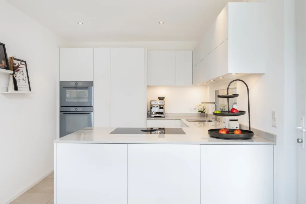 Moderne, helle Küche mit Kochinsel, weißen Einbauschränken und integrierten Geräten in einem Einfamilienhaus von Atmoshaus.