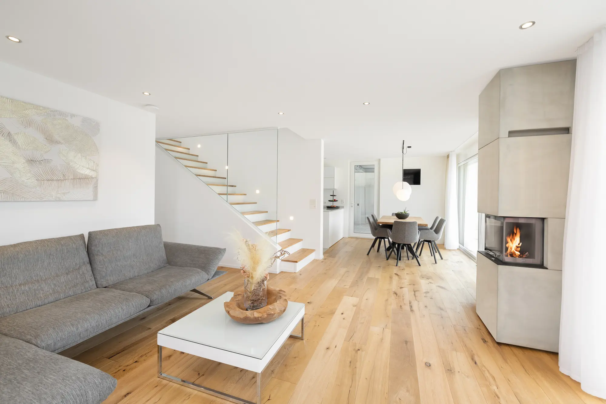 Offener Wohn- und Essbereich mit Sofa, Treppe, Kamin und Holzboden.